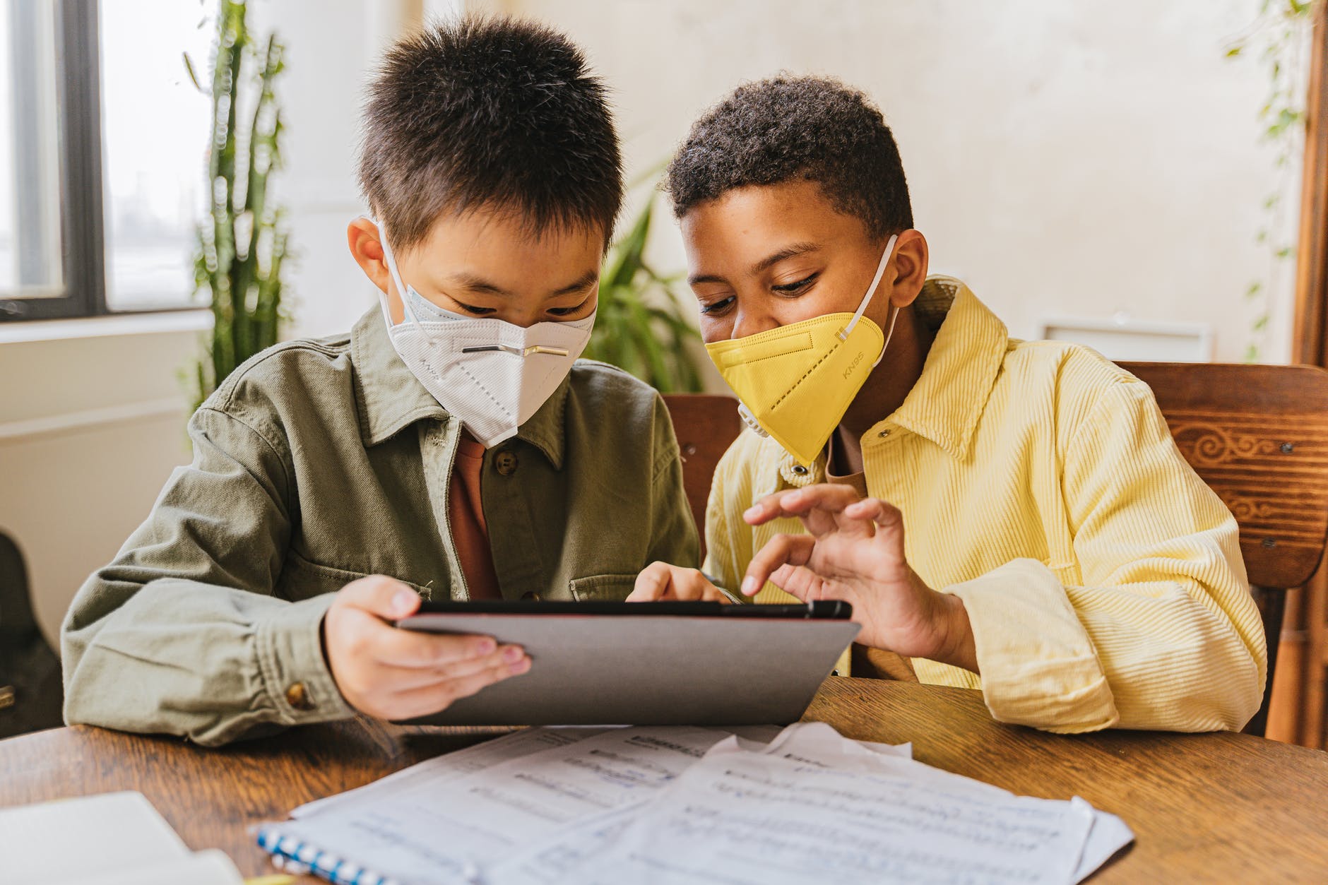 children wearing face masks looking at the screen of tablet